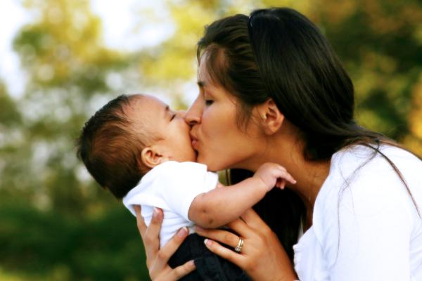 mum kissing baby on cheek with green foliage in the background