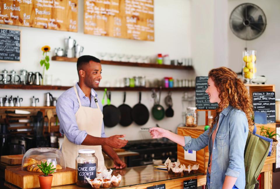 A female customer hands a credit card to a male staff member at the front counter of a cafe