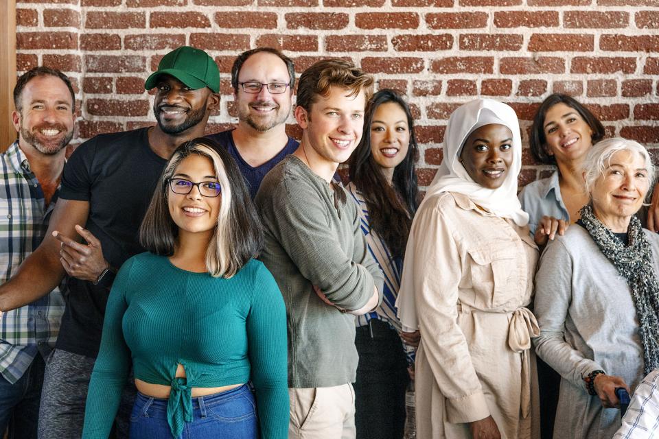Group of people of all ages and nationalities standing against a red brick wall