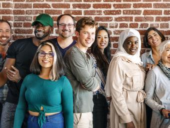 Group of people of all ages and nationalities standing against a red brick wall