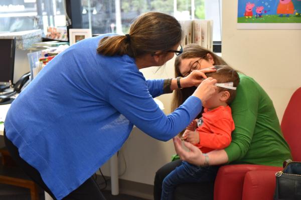 Maternal child health nurse measuring childs head with the child sitting on their mum's lap