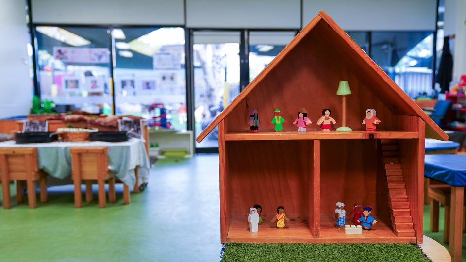 image of dolls house at Early Years MC square with dolls in it. The rest of the kinder room is slightly blurred in the background