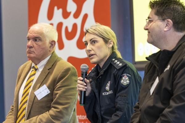3 people sit on stage including Victoria Police member who speaks into a microphone