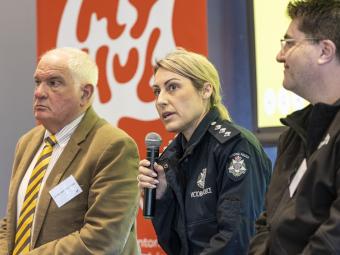3 people sit on stage including Victoria Police member who speaks into a microphone