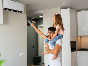 Father with little daughter on shoulders turn on reverse cycle air conditioner using remote control